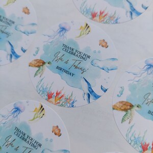 May include: Round blue and white thank you stickers with a watercolor design featuring sea creatures like a whale, turtle, jellyfish, and fish. The text on the stickers reads "Thank you for celebrating Isla & Tobias' Birthday."