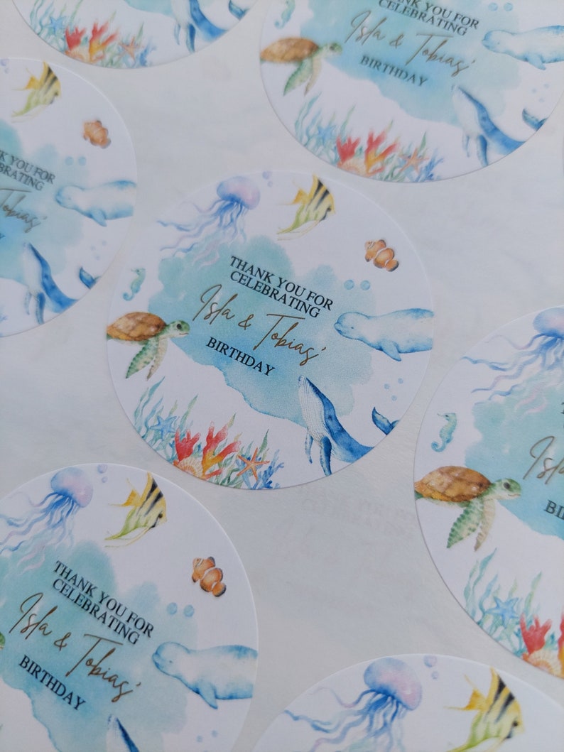 May include: Round blue and white thank you stickers with a watercolor design featuring sea creatures like a whale, turtle, jellyfish, and fish. The text on the stickers reads "Thank you for celebrating Isla & Tobias' Birthday."
