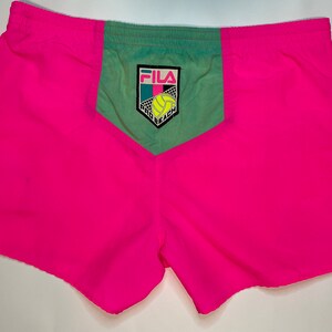 May include: Pink and green athletic shorts with a Fila logo and "Pad Beach" text on the back pocket.