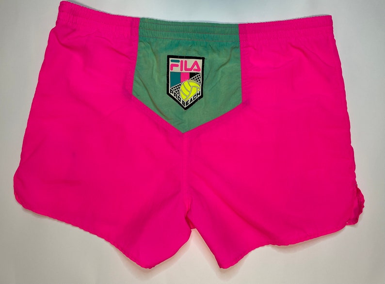 May include: Pink and green athletic shorts with a Fila logo and "Pad Beach" text on the back pocket.