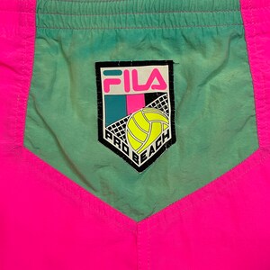 May include: Pink and green athletic shorts with a Fila logo and the words "Pro Beach" on the front.