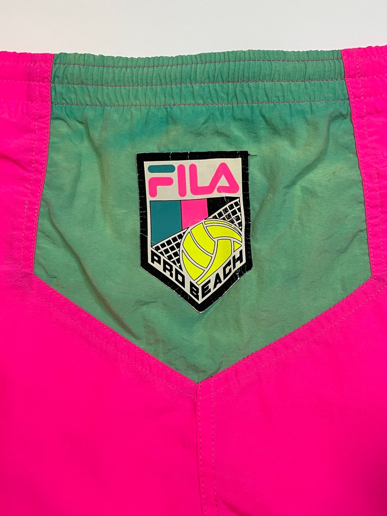 May include: Pink and green athletic shorts with a Fila logo and the words "Pro Beach" on the front.