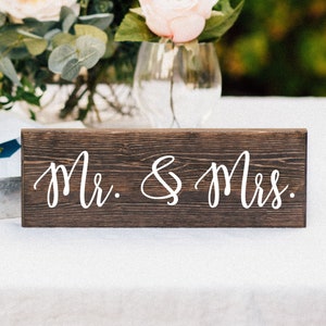 May include: A rustic wooden sign with the text "Mr. & Mrs." in white cursive lettering.