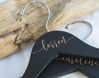 May include: Two black wooden hangers with gold lettering. The top hanger says "lorren" and the bottom hanger says "carole".