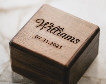 May include: A dark brown wooden ring box with the name "Williams" and the date "07.31.2021" engraved on the top.