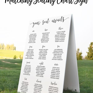 May include: White sign with black text, titled "Matching Seating Chart Sign" with the words "your seat awaits" in cursive. The sign lists names for a wedding reception seating chart, with table numbers one through twelve.
