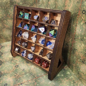 May include: A wooden dice display rack with multiple compartments, filled with various polyhedral dice in different colors and materials. The rack is made of dark wood and has a slanted design.