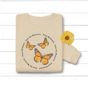 May include: A beige t-shirt with a circular design featuring three monarch butterflies and the text "Save the Monarchs Plant Milkweed" repeated around the circle.