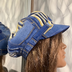 Puede incluir: Una gorra de estilo newsboy confeccionada con parches de tela vaquera en varios tonos de azul, con paneles a rayas en contraste de color amarillo, blanco y azul oscuro. La gorra presenta costuras en zigzag visibles en las uniones.