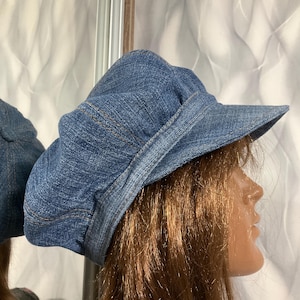 Puede incluir: Una taza de cerámica blanca con un asa negra y el texto "But First, Coffee" en negrita negra. La taza se encuentra sobre un fondo borroso, sugiriendo un ambiente acogedor.