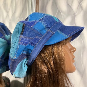 May include: A patchwork denim hat in shades of blue, with a curved brim. The hat is constructed from various denim pieces, stitched together with contrasting thread. The hat is displayed on a mannequin head.