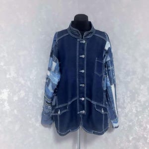 Puede incluir: Chaqueta vaquera azul oscuro con costuras blancas y mangas patchwork. La chaqueta tiene cuello mandarín, cierre de botones y dos bolsillos delanteros. Las mangas están hechas de varios parches de mezclilla azul.