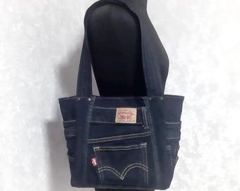 Könnte beinhalten: Eine dunkelblaue Denim-Tragetasche mit rechteckiger Form und zwei Schultergurten. Die Tasche hat mehrere Taschen, sichtbare Nähte und ein rechteckiges Etikett mit Text. Das Levi's-Logo ist sichtbar.
