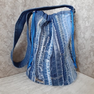 May include: A denim bucket bag with a drawstring closure and a shoulder strap. The bag is made from repurposed blue jeans, featuring visible seams and frayed edges. The drawstring and strap are a vibrant blue.