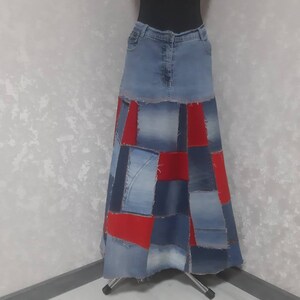 May include: A patchwork denim skirt with a light blue denim waistband. The skirt features a patchwork design of various shades of blue denim and red fabric panels. The skirt is displayed on a mannequin.