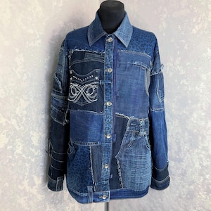May include: A patchwork denim jacket in various shades of blue. The jacket features a collared neckline, button-up front, and multiple denim patches. Some patches have white embroidered details and leopard print accents. The jacket is displayed on a black mannequin.