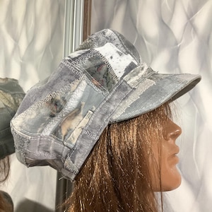 May include: A grey patchwork cap featuring various shades of grey and white fabric panels with visible frayed edges and decorative stitching. The cap has a structured crown and a stiffened brim, constructed from multiple textured fabric pieces.