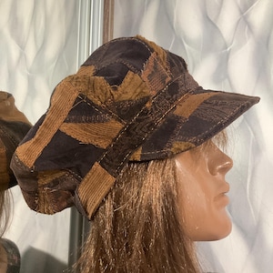 May include: A newsboy cap constructed from a patchwork of various fabrics in shades of dark brown, tan, and copper. The hat features a structured brim and a multi-textured design with visible stitching connecting the different fabric panels.
