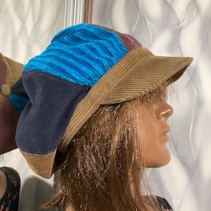 May include: A brown corduroy hat with a blue, purple, and black patchwork design. The hat has a wide brim and a slightly rounded crown.