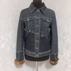 Può includere: Giacca di jeans blu scuro con colletto classico e chiusura con bottoni. La giacca presenta più tasche, cuciture decorative e dettagli distressed. I polsini sono rifiniti con pelliccia marrone. Un capo di abbigliamento esterno elegante.