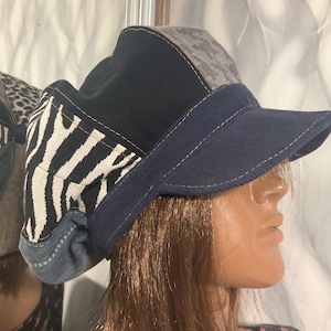 May include: A black, gray, and white patterned cap with a blue brim. The cap is made of different fabrics and has a unique design.