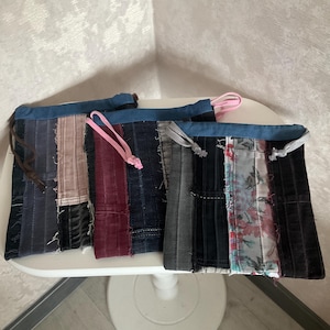 Può includere: Tre pochette patchwork con pannelli in denim e tessuto in vari colori, tra cui blu, grigio, rosa e stampe floreali. Ogni pochette ha una chiusura con coulisse con un cordino di colore diverso.