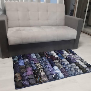 May include: A blue and purple tie rug made from recycled ties. The rug is made up of individual tie knots, creating a unique and textured surface.