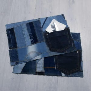 Peut inclure: Deux sets de table en denim composés de pièces de denim patchwork dans diverses nuances de bleu. Chaque set de table a une poche en denim bleu foncé et l'un d'eux a une serviette blanche avec une fourchette et un couteau.