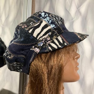 May include: A patchwork newsboy cap featuring a variety of fabric textures and patterns, including black and white zebra stripes, dark blue corduroy, and floral prints. The panels are joined with visible zigzag stitching in a light tan thread.