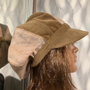 May include: A brown corduroy and pink patterned fabric newsboy cap with a brim.