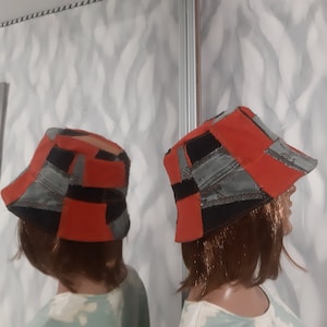 May include: Two patchwork bucket hats. The hats feature a mix of red, black, and grey denim patches. The hats are displayed on mannequins. The hats have a brim and a rounded crown.