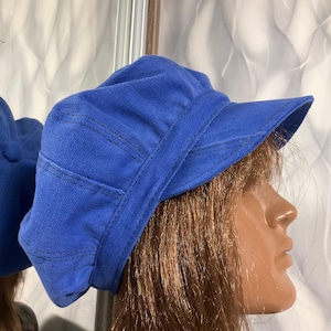 Może przedstawiać: Niebieska czapka typu newsboy z dżinsu. Czapka ma zaokrągloną koronę i jest ozdobiona widocznymi szwami. Kapelusz jest w jednolitym, żywym niebieskim kolorze i wydaje się być wykonany z wytrzymałej tkaniny.