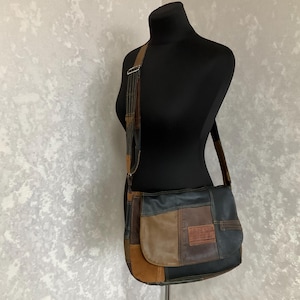 Könnte beinhalten: Eine Messenger-Tasche aus Patchwork-Leder mit Schulterriemen. Die Tasche hat eine Vielzahl von braunen, beigen und schwarzen Lederflicken. Die Tasche wird auf einer schwarzen Schaufensterpuppe präsentiert.