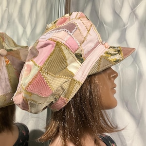 Może przedstawiać: Patchworkowa czapka w odcieniach różu, beżu i zieleni. Czapka ma geometryczny wzór wykonany z różnych tkanin. Rondo i opaska są w jednolitym różowym kolorze. Unikalny, ręcznie robiony dodatek.