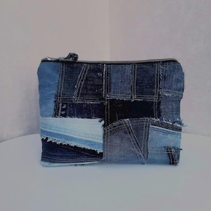 Op de afbeelding: Een rechthoekig denim etui met een ritssluiting. De etui is gemaakt van verschillende tinten blauwe denim patches, waardoor een patchwork ontwerp ontstaat. De ritssluiting is donkergrijs. De etui staat op een wit oppervlak.