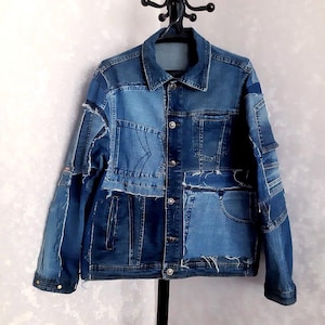May include: A patchwork denim jacket in various shades of blue. The jacket features a collared neckline, button-down closure, and multiple pockets. The design incorporates different denim pieces, creating a unique, textured look. The jacket is hanging on a black hanger.
