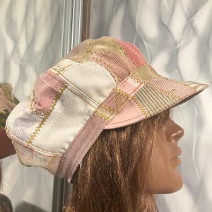 May include: A patchwork newsboy cap constructed from various fabric panels in shades of pink, cream, and beige. The cap features visible yellow zigzag stitching along the seams, combining corduroy and smooth textile textures with a stiffened brim.