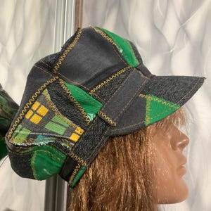 Puede incluir: Una gorra de patchwork confeccionada con paneles de tela vaquera gris oscuro y verde vibrante. El diseño presenta un patrón de cuadros en amarillo, verde y negro, acentuado con costuras en zigzag amarillas visibles en las uniones.