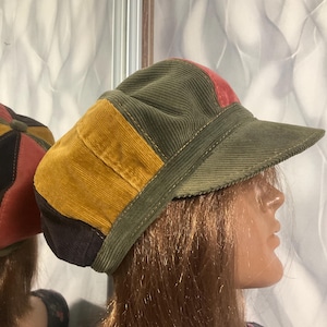 May include: A corduroy baseball cap with a patchwork design. The cap features panels of olive green, mustard yellow, and red. The brim is olive green. The cap is displayed on a mannequin head.