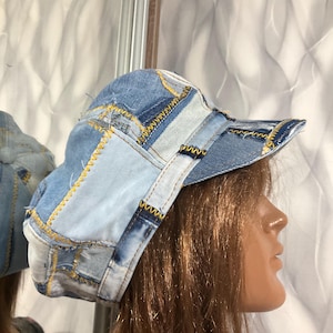 Puede incluir: Gorra de béisbol de mezclilla patchwork con paneles de mezclilla azul claro y medio. La gorra presenta costuras amarillas y una visera curva. El sombrero está diseñado con una estética casual y vintage.