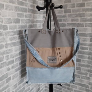 Puede incluir: Un bolso tote multicolor con la parte superior gris, el centro beige y la parte inferior de mezclilla azul claro. El bolso cuenta con una correa de hombro de mezclilla y está adornado con remaches metálicos. El texto "freesoul" es visible en una pequeña etiqueta.