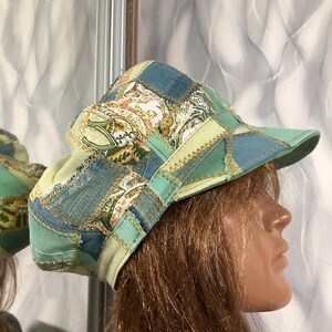 Puede incluir: Una gorra de patchwork que presenta una variedad de paneles de tela en tonos verde azulado, verde claro y azul. El sombrero está construido con costuras en zigzag visibles que conectan las diferentes piezas textiles, incluyendo secciones con un patrón floral.