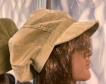 May include: A tan corduroy newsboy cap with a wide brim. The cap is folded down on one side and has a slightly slouchy fit.