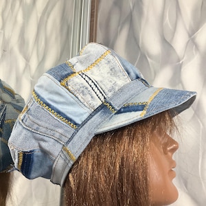 May include: A patchwork denim newsboy cap in shades of blue, with yellow stitching. The cap features a short brim and a rounded crown, constructed from various denim pieces. The design gives a vintage, upcycled aesthetic.