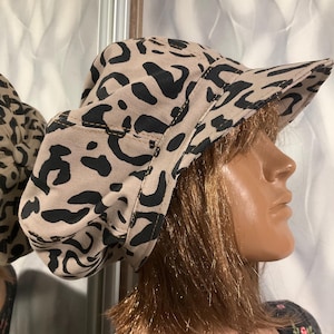 May include: A beige and black leopard print hat with a short brim. The hat is made of a soft fabric and has a rounded crown. The hat is displayed on a mannequin head.