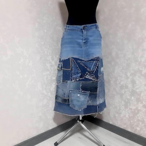 May include: A denim skirt with a patchwork design. The skirt is a light to medium blue color with darker blue patches and pockets sewn together. The skirt is displayed on a mannequin.