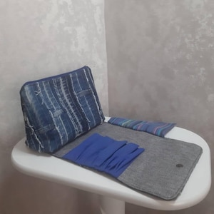 May include: A blue and gray travel organizer with a zippered pouch, a gray mat, and blue accents. The pouch has a denim-like appearance with white vertical stripes. The organizer is open and displayed on a white table.
