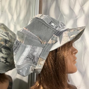 Puede incluir: Una gorra de patchwork gris confeccionada con varios tonos de mezclilla y retazos de tela. El sombrero presenta bordes deshilachados visibles, costuras en zigzag expuestas y una visera estructurada. El diseño incorpora paneles grises.