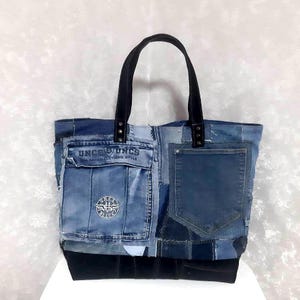 May include: A patchwork denim tote bag with black leather handles and a black base. The bag features two denim pockets and a patch with the text "UNCS UNLIMITED CLOTHING STYLE".