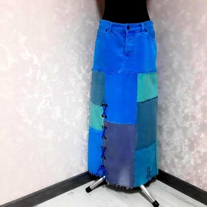 Könnte beinhalten: Ein langer Jeansrock in Blautönen, der aus Patchwork-Quadraten gefertigt ist. Der Rock hat einen klassischen Jeansbund und ein Schnürdetail an der Seite. Der Rock wird auf einer Schaufensterpuppe präsentiert.